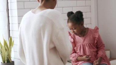 Annesi mutfakta yemek pişirirken neşeli Afrikalı küçük kız konuşuyor.