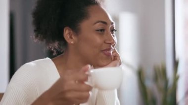 Gülümseyen Afrikalı kadın elinde fincanla konuşuyor.