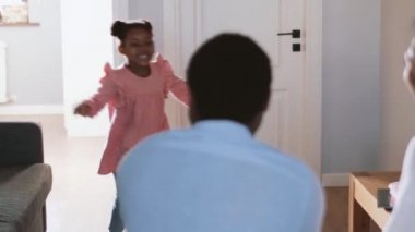 Olumlu küçük Afrikalı kız koşuyor ve anne babasına sarılıyor.