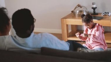 Konsantre olmuş genç Afrikalı kız evde ebeveynler televizyon izlerken yere bir şeyler çiziyor.