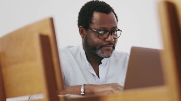 Θετικός Αφρικανός Επιχειρηματίας Γράφει Κάτι Χαρτί Από Φορητό Υπολογιστή Στο — Αρχείο Βίντεο