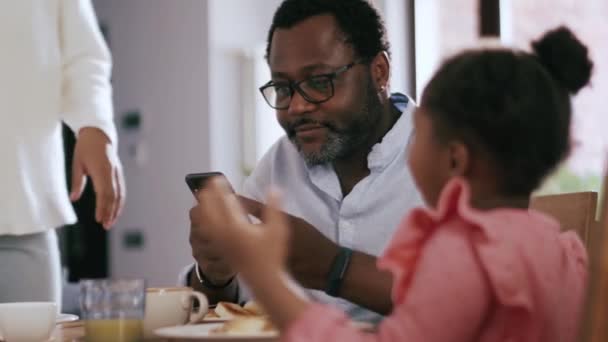 Χαμογελώντας Αφρικανός Κοιτάζοντας Τηλέφωνο Μετά Πρωινό Την Οικογένειά Του Στο — Αρχείο Βίντεο