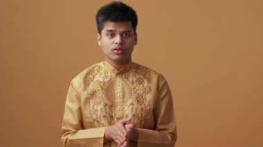 Ulusal giysili kendine güvenen Hintli adam turuncu stüdyoda kamerayla konuşuyor.