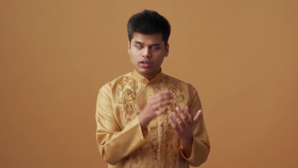 穿着民族服装的积极的印度人靠橙色工作室里的手指指望着 — 图库视频影像