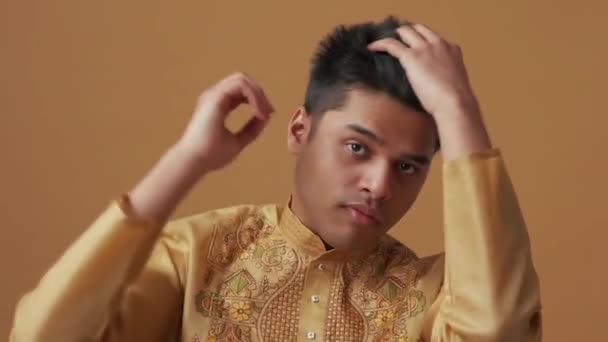 一位身穿民族服装的严肃的印度人在橙色工作室的摄像机前修正了自己的外表 — 图库视频影像