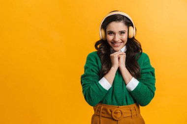 Sarı duvardan izole edilmiş kulaklıkla müzik dinleyen mutlu, genç, sıradan, beyaz bir kadın.