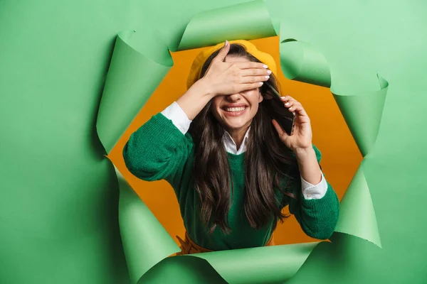若いです白い笑顔女性Peekingアウトホール隔離上の緑の背景通話上の携帯電話カバー目 — ストック写真