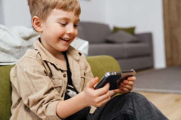 Glad Pojke Barn Som Håller Mobiltelefon Medan Sitter Vardagsrummet — Stockfoto