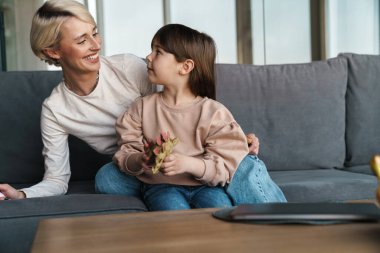 Mutlu genç anne ve küçük kızı oturma odasında bir kanepede kaynaşıyorlar.