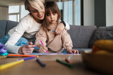 Genç anne ve anaokulu kızı oturma odasında resim çiziyor, sarılıyorlar.