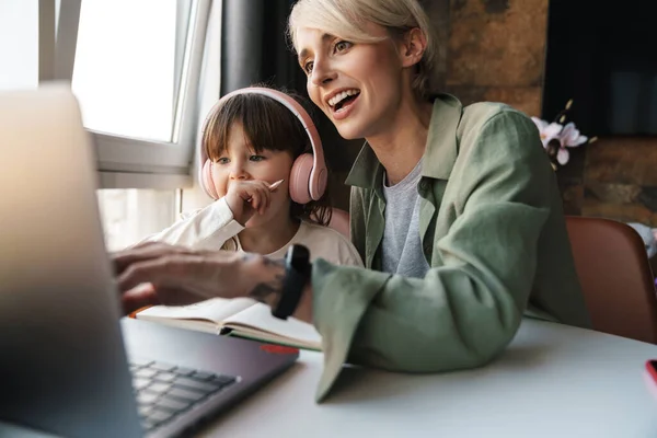 快乐的母亲帮助女儿做功课 使用笔记本电脑 在隔离期间学习 小女孩用耳机听老师讲课 — 图库照片