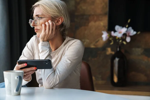 Enttäuschte Junge Frau Freizeitkleidung Mit Handy Küchentisch Mit Tasse Kaffee — Stockfoto