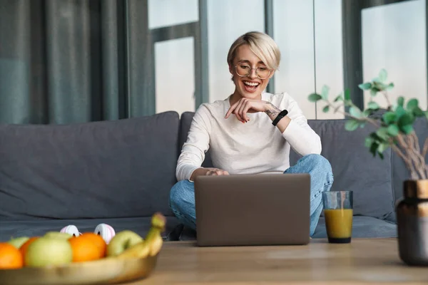 笑顔中年ブロンド女性勉強オンライン経由ラップトップコンピュータでザリビングルーム — ストック写真