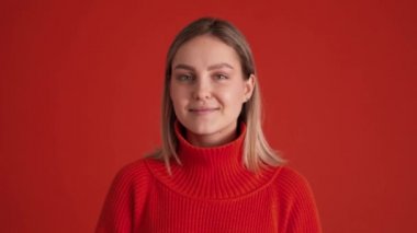 Kırmızı kazak giyen neşeli kadın kırmızı stüdyoda kameraya bakıyor.