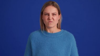 Mavi kazak giyen kızgın kadın mavi stüdyoda kameraya bağırıyor.