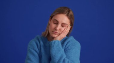 Mavi kazak giyen yorgun kadın mavi stüdyoda derin bir nefes alıyor.