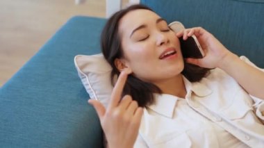 Kanepede telefonla konuşan gülen Asyalı kadın.