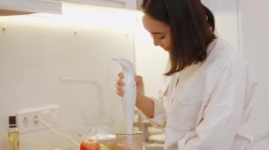 Pozitif Asyalı kadın mutfakta muzlu milkshake yapıyor.