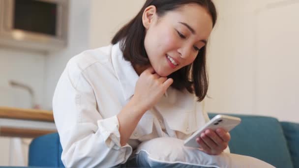 Positivo Asiático Mujer Mensajes Texto Por Teléfono Sofá — Vídeo de stock