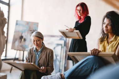 Genç çok ırklı öğrenciler sanat okulunda derste alçı büstü çiziyorlar.