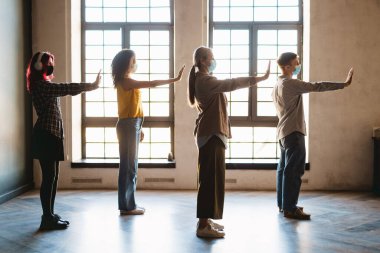 Olgun öğretmen ve maskeli öğrenciler okulda kapalı alanda egzersiz yapıyorlar.