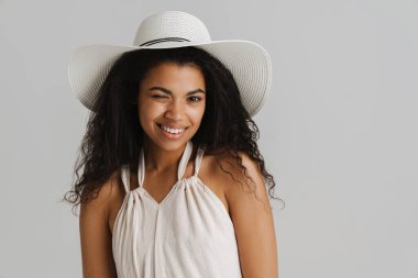 Beyaz arka planda izole edilmiş, gülümseyen ve kameraya göz kırpan şapkalı siyahi genç kadın.