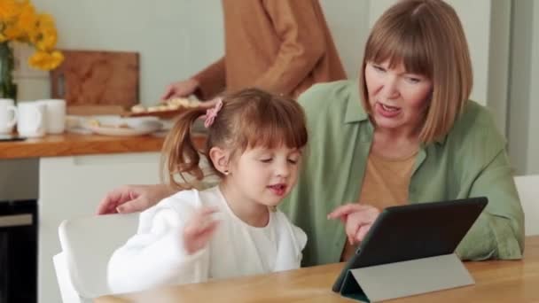 Skoncentrowana Babcia Ogląda Coś Tablecie Rozmawia Wnuczką Kuchni — Wideo stockowe