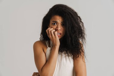 Beyaz arka planda izole edilmiş kameraya bakarken parmaklarını ısıran siyah, korkmuş kadın.