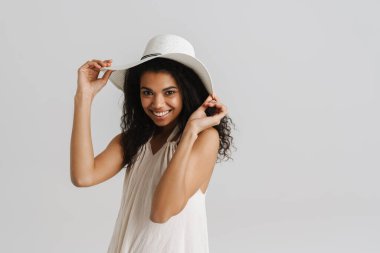 Şapkalı genç bir kadın gülümsüyor ve beyaz arka planda izole edilmiş kameraya bakıyor.