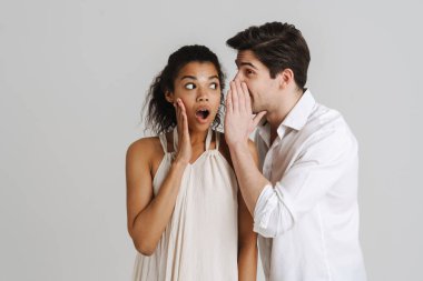 Şok olmuş, çok ırklı genç bir çift gri arka planda tek başına dikilip sırlarını anlatıyor.