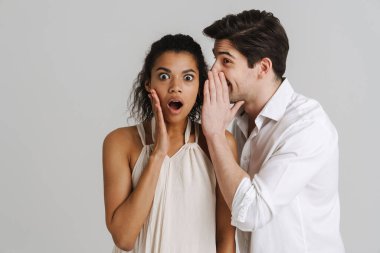 Şok olmuş, çok ırklı genç bir çift gri arka planda tek başına dikilip sırlarını anlatıyor.