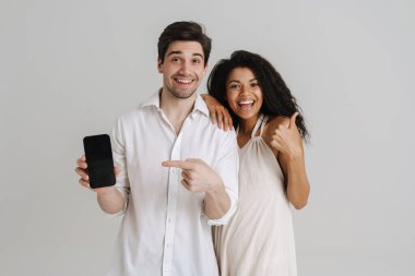 Beyaz duvardan izole edilmiş cep telefonlarını işaret eden çok ırklı erkek ve kadın.