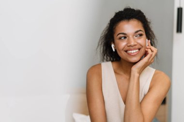 Mutlu, genç Afrikalı bir kadın yatak odasında oturmuş kulaklıkla müzik dinliyor.