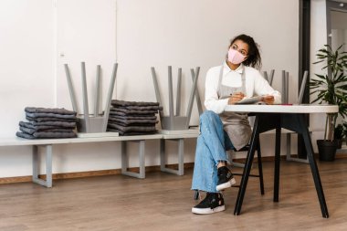 Yüz maskesi takan genç zenci garson iş yerindeki panoya notlar yazıyor.