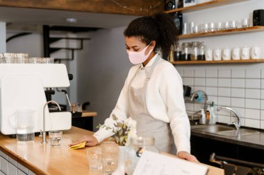 Yüz maskeli genç zenci garson, kafeteryada çalışıyor.