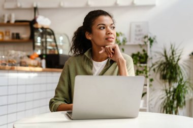 Genç siyahi kadın, kafede otururken dizüstü bilgisayarla çalışıyor.