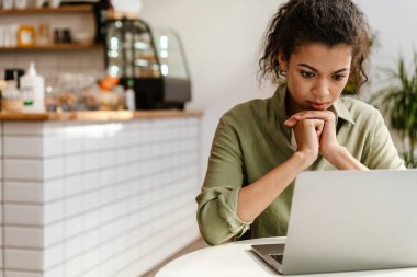 Genç siyahi kadın, kafede otururken dizüstü bilgisayarla çalışıyor.