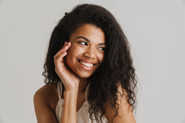 Smiling young african woman in casual wear standing over isolated gray background looking aside