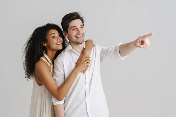 Young Multiracial Couple Hugging Pointing Finger Aside Isolated White Background — Stock Photo, Image