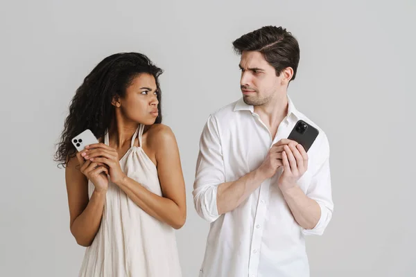 Young Multiracial Couple Frowning While Using Mobile Phones Isolated White — Stock Photo, Image