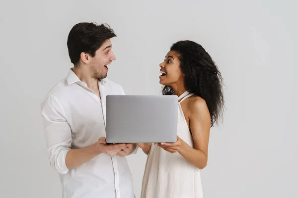 多种族夫妇拿着笔记本电脑摆出一副兴奋的样子 在白色的背景上相互凝视着对方 — 图库照片