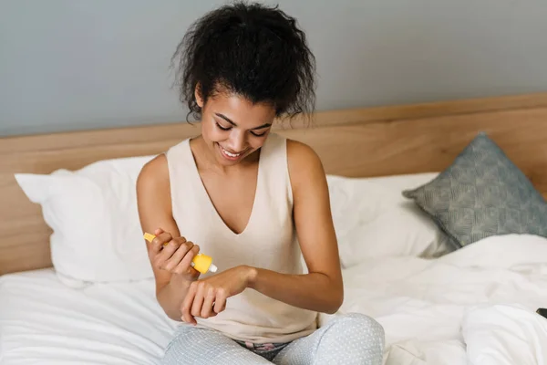 Joven Mujer Negra Sonriendo Aplicando Crema Manos Mientras Está Sentada — Foto de Stock