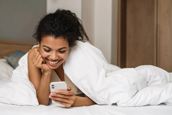 Joven Mujer Negra Sonriendo Usando Teléfono Inteligente Mientras Está Acostada — Foto de Stock