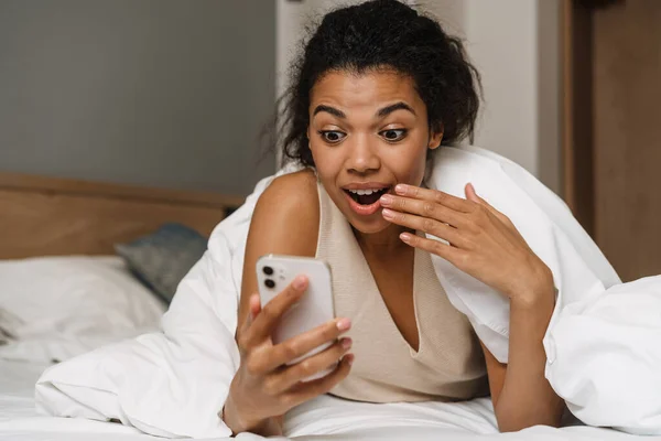 Fiatal Fekete Meglepett Használ Okostelefon Miközben Feküdt Ágyban Alvás Után — Stock Fotó