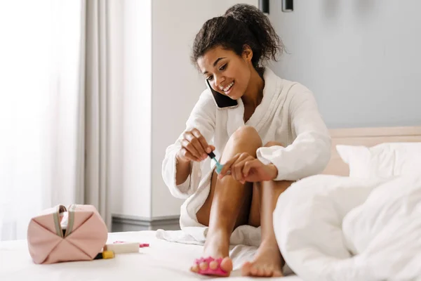 Sorridente Giovane Donna Africana Accappatoio Seduta Letto Dipingere Unghie Camera — Foto Stock