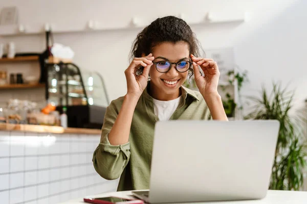 坐在室内咖啡店时 戴着眼镜 拿着笔记本电脑工作的年轻黑人妇女 — 图库照片