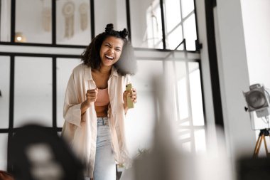 Genç, mutlu, Afro-Amerikan kadın elinde akıllı telefon dansı ile evde eğleniyor.