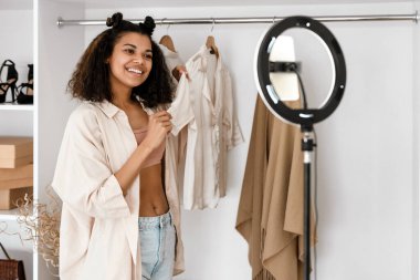 Giysilerini gösteren siyahi bir kadın gardıropta cep telefonundan selfie çekerken.