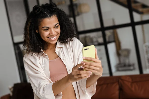 Musta Nuori Nainen Hymyilee Ottaessaan Selfie Matkapuhelimeen Kotona — kuvapankkivalokuva