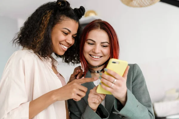 Молодые Многорасовые Две Женщины Улыбаются Используя Мобильный Телефон Дома — стоковое фото